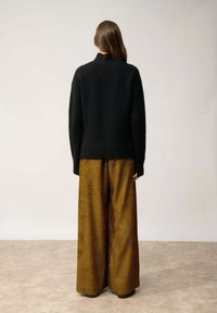 Czarny sweter dzianinowy z wysokim kołnierzem i prążkowanym wykończeniem, w połączeniu z brązowymi szerokimi spodniami z korduroju w pionowe paski.