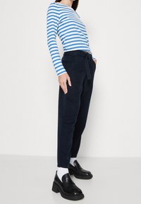 Blå och vit randig långärmad tröja, mörk marinblå tapered byxor med bälte, svarta klackloafers, vita strumpor. Slät tygtextur.