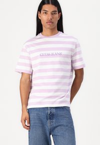 Stripet kortermet t-skjorte i lavendel og hvit; har "GUESS JEANS"-logoen i lilla broderi på brystet. Mykt bomullsstoff.