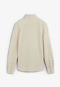 Camisa beige de manga larga con puños abotonados, cuello clásico y espalda lisa, presentada plana sobre un fondo blanco.