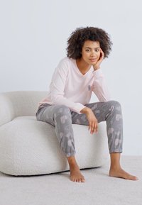 Ljusrosa långärmad topp med en liten hjärtdesign, tillsammans med grå byxor med hjärttryck, elastiska ärmslut och mjuk textur.