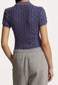 Lila stickad pikétröja med kabelstruktur och korta ärmar, kombinerad med grå mjukisbyxor med resår i midjan.