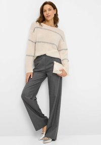 Cremefarbener Pullover mit grauen Streifen, kombiniert mit grauen weiten Hosen. Accessoires sind eine kleine cremefarbene Clutch und silberne flache Schuhe.