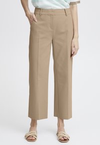 Pantalons beige à jambes larges avec une texture lisse, un léger éclat et des poches avant. Design court mettant en valeur des sandales confortables.