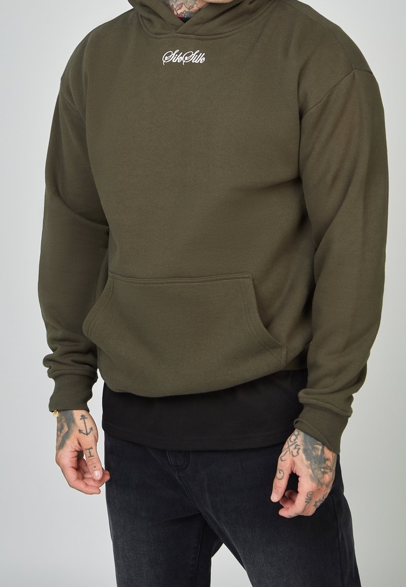 Sweat à capuche vert olive avec une poche avant, des poignets côtelés et un logo brodé sur la poitrine, superposé à un t-shirt noir.
