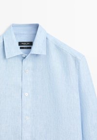 Chemise en lin bleu clair à manches longues avec col pointu et boutons blancs, étiquetée Massimo Dutti.