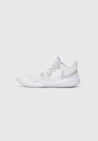Bílé sportovní boty s vrchní částí z síťoviny, se stříbrným logem Nike, texturovanou podrážkou a bílými šňůrkami. Kulatá špička a polstrovaný límec.