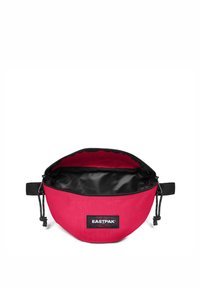 Bum bag rossa Eastpak con cerniera nera aperta, che mostra l'interno foderato di nero e la tracolla nera regolabile su sfondo bianco.