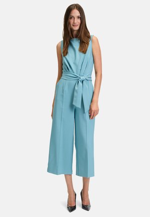 Una tuta senza maniche in tessuto azzurro chiaro, con un corpetto aderente, vita cintata con nodo frontale e pantaloni a gamba larga e cropped.