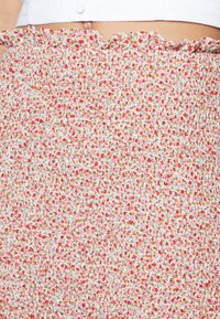 Saia floral com pregas e cintura franzida, apresentando um padrão de flores vermelhas e rosas sobre um fundo claro. Tecido suave e texturado.