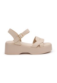 Sandalias de plataforma beige con correas entrelazadas y hebilla ajustable en el tobillo. Presentan una textura suave y una base robusta y ligera.