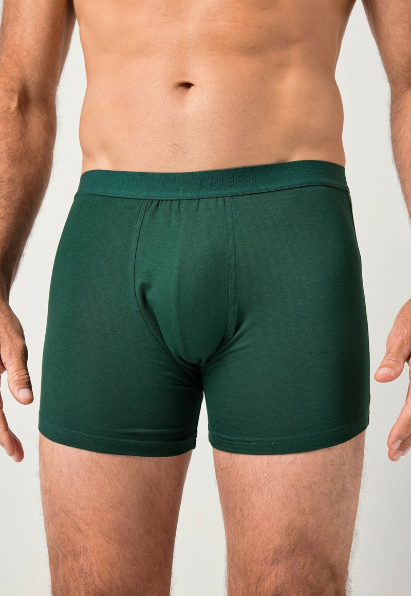 Boxers ajustados de color verde oscuro, hechos de una tela suave y elástica. Presentan un diseño ceñido y un soporte en la parte frontal. La cinturilla es elástica y cuenta con una marca.