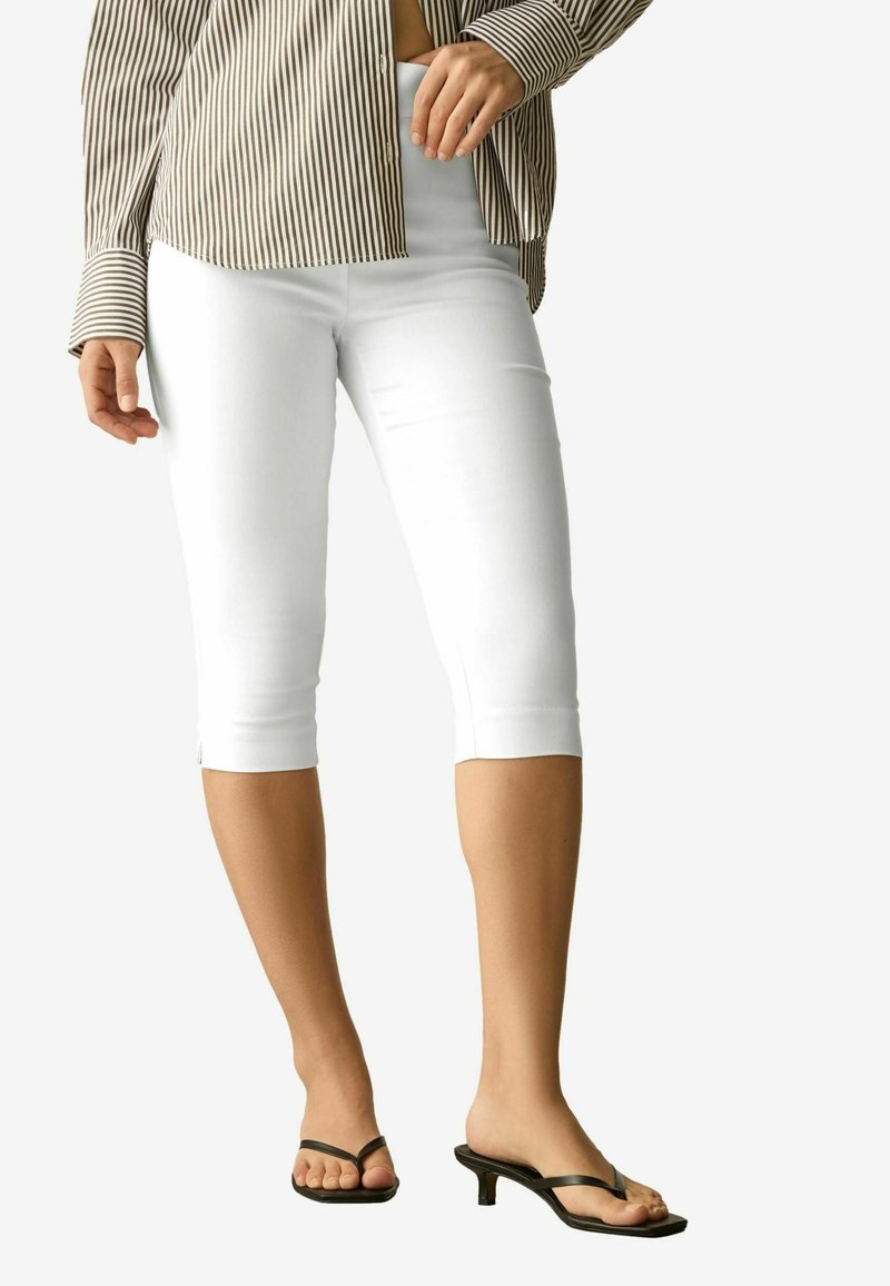 Hvide cropped leggings med en tætsiddende design, glat tekstur og afsluttede manchetter, parret med sorte flip-flop sandaler. Stribet skjorte ovenfor.