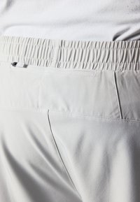 Ανοιχτό γκρι παντελόνι με ελαστική μέση και πίσω τσέπη με φερμουάρ; λείο ύφασμα με διακριτή υφή, με ραμμένες ραφές.