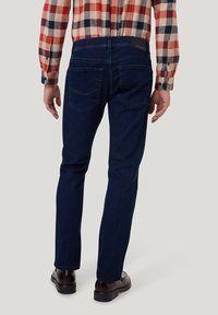 Donkerblauwe jeans met een slim fit, voorzien van twee achterzakken en subtiele stikdetails, gecombineerd met een geruit overhemd met knopen.