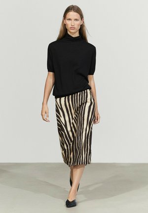 Donna che cammina indossando una maglietta nera a maniche corte e una gonna midi beige e nera a strisce zebrate con ballerine nere.