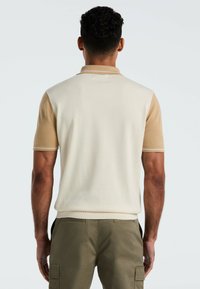 Kurzarm-Poloshirt in Creme mit hellbraunen Schulterpaneelen. Glatte Textur, gerippter Kragen und Bündchen, taillierte Passform und dezente Stichdetails.