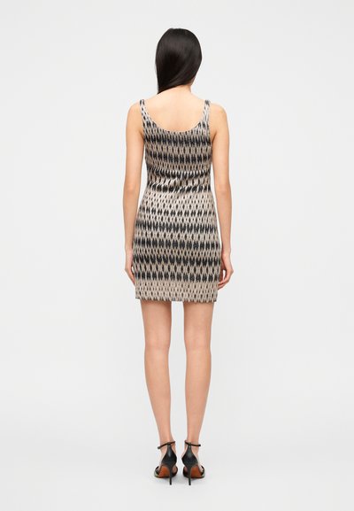 Μίνι φόρεμα χωρίς μανίκια με γεωμετρικό μοτίβο σε μαύρο και μπεζ, εφαρμοστή γραμμή, μήκος έως το μέσο του μηρού, λεία υφή. Συνδυασμένο με μαύρα πέδιλα ψηλού τακουνιού.