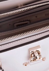 Borsa in pelle bianca con hardware dorato, dotata di più scomparti con zip e una superficie liscia. Gli accenti includono cuciture sottili.