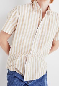 Koszula z krótkim rękawem na guziki w jasnobeżowe i białe pionowe paski. Wykonana z lnu o miękkiej fakturze; posiada klasyczny kołnierzyk.