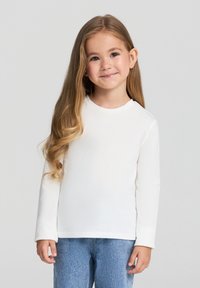 Biała, długosleeve koszulka z okrągłym dekoltem, o miękkiej fakturze i luźnym kroju, zestawiona z niebieskimi dżinsami.