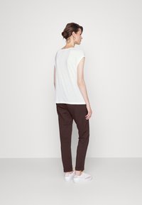 Top branco de mangas curtas combinado com calças castanhas justas e sapatilhas brancas. O tecido parece suave com um ajuste casual e um design simples.