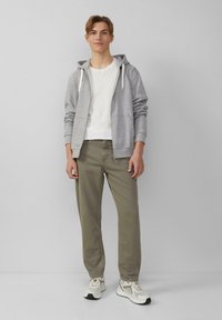 Szara bluza rozpinana z białymi sznurkami, biała koszulka, oliwkowe spodnie oraz jasnoszare trampki z białymi akcentami. Prosty i casualowy design.