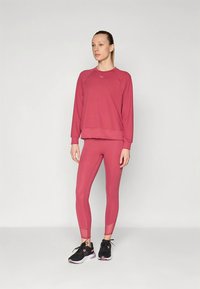 Completo rosa composto da maglione e leggings in un tessuto liscio. Il maglione presenta una scollatura rotonda e polsini a coste; i leggings hanno un design aderente con lunghezza corta.