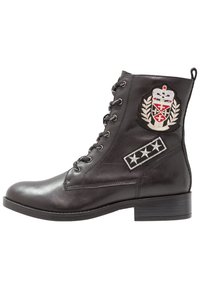 Mustat nahkaiset nilkkasaappaat nauhaketjulla, joissa on kuninkaallinen logo ja emblemipatchi sekä koristeellinen tähden kuvio sivuilla.