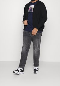 Svart cardigan, marinblå grafisk t-shirt, grå jeans och svarta och vita sneakers. Akrylkardigans med knappar, avslappnad outfit.