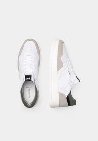 Sneaker atletici bianchi con pelle perforata, dettagli in suede grigio e verde, lacci piatti e una spessa suola in gomma bianca.