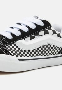 Sneaker low-top con motivo a scacchi in bianco e nero, lacci bianchi e suola in gomma bianca con dettaglio a striscia nera.