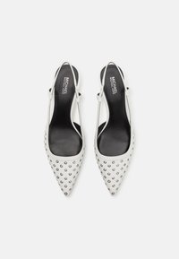 Scarpe slingback bianche con punta a forma affusolata, caratterizzate da dettagli in metallo argentato sul puntale e una fodera interna nera liscia.