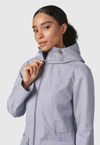 Giacca a vento lavanda chiaro con zip frontale, cappuccio regolabile e due tasche. Presenta una texture liscia e un design aderente.