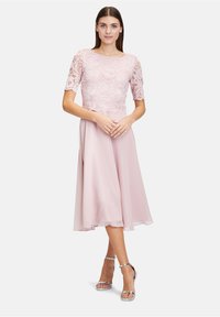 Różowa sukienka z koronkowym gorsetem, krótkimi rękawami i zwiewną spódnicą z szyfonu. Srebrne sandały na kostkę uzupełniają strój.