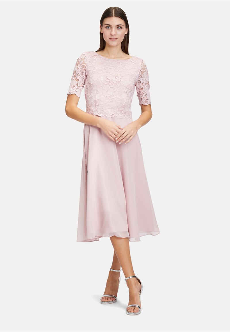 Różowa sukienka z koronkowym gorsetem, krótkimi rękawami i zwiewną spódnicą z szyfonu. Srebrne sandały na kostkę uzupełniają strój.