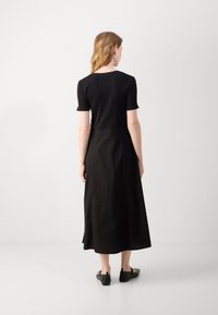 Black mid-length dress with short fitted sleeves, featuring a smooth texture and zipper detail at the back. Worn with flat black shoes.