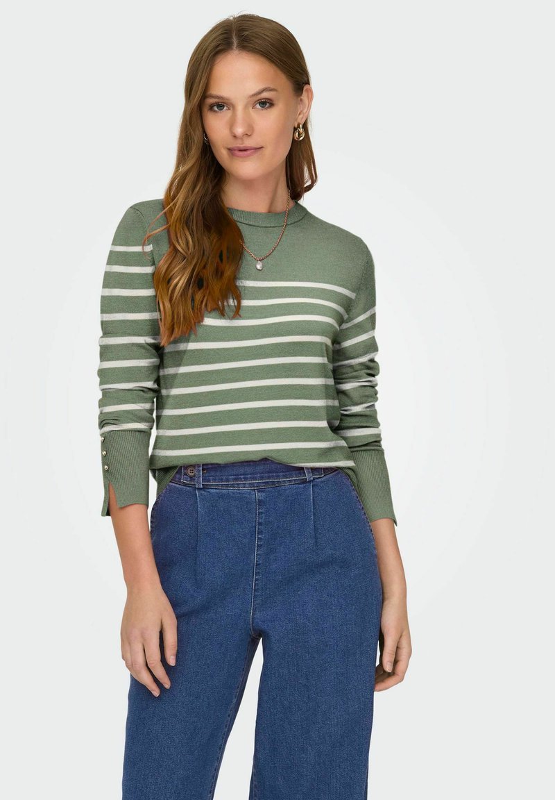 Pull rayé vert avec un col rond et des fentes sur les manches. Associé à un pantalon en denim bleu taille haute.