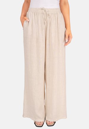 Pantalon beige ample en lin avec taille élastique et cordelette, porté avec des sandales noires à bout carré et un haut blanc.