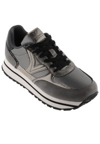 Zapatilla atlética gris con una combinación de superficies mate y brillantes, cordones negros y una suela blanca gruesa con una franja de acento negra.