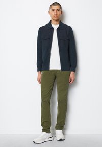 Marinblå zip-up jacka med texturerad stickning och två bröstfickor, tillsammans med olivgröna byxor och vita sportskor. Enkel, modern design.