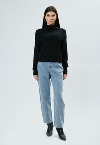 Schwarzer Strickrollkragenpullover mit Zopfmuster, kombiniert mit hellblauen lockeren Jeans und schwarzen Ankle Boots.