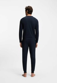 Completo da casa blu navy in tessuto morbido, composto da maglia a maniche lunghe e pantaloni aderenti con polsini a costine, mostrato di spalle.