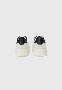 Hvite sneakers med semsket tekstur, kontrasterende svart lærhælkappe og tykk mellomsåle. Rund form og minimalistisk design.
