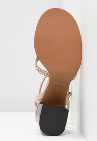 Sandale avec semelle couleur cognac, talon bloc noir et brides tressées beiges, taille 38, positionnée semelle vers le haut sur fond blanc.