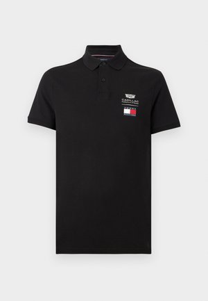 Fekete rövid ujjú póló kétgombos patenttal, Cadillac Formula 1 Csapat logóval és Tommy Hilfiger zászlóval a bal mellrészen.