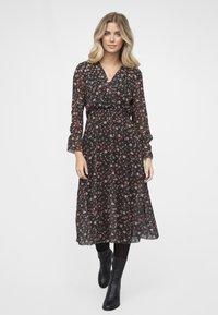 Svart blomsterkjole med lange ermer, midi-lengde, samlet midje, og små røde og gule blomster. Brukt med svarte knelangstøvelsko.