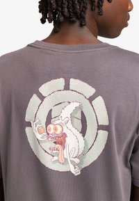 Camiseta de algodón gris con un estampado colorido de un personaje salvaje en la parte posterior, que presenta expresiones faciales exageradas y elementos llamativos.
