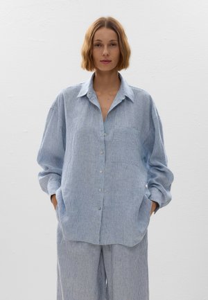 Camicia a righe blu chiaro con taschino sul petto, vestibilità comoda e maniche lunghe. Abbinata a pantaloni ampi coordinati.
