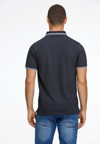 Polo shirt bleu marine foncé à manches courtes, avec des accents rayés blancs et bleu clair sur le col et les ourlets des manches.